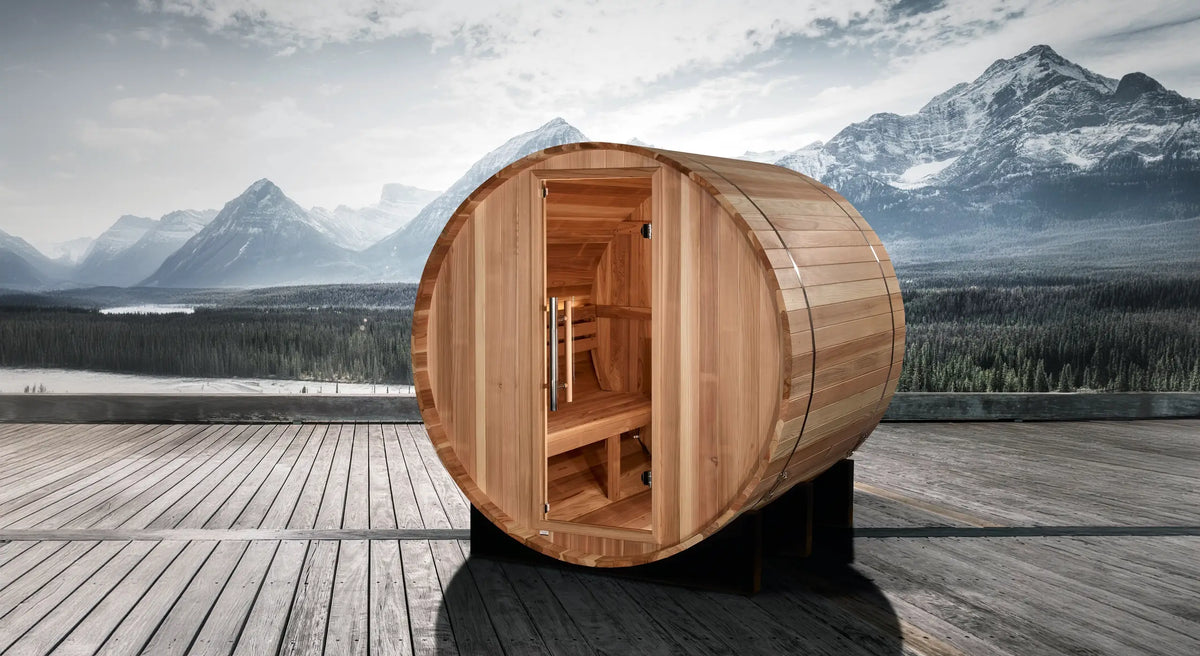 Golden Designs St. Moritz model barrel shaped sauna with a 2 person capacity which is built for outside use on a wooden dock overlooking a lake with snowy mountains in the distance